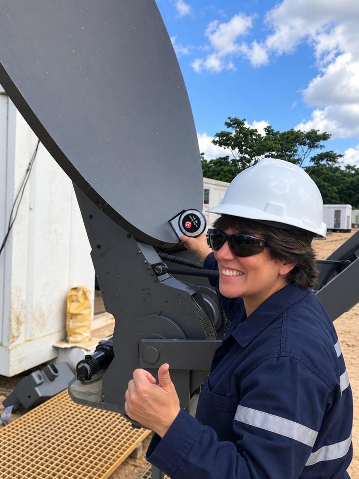 María Quintero, con casco y overol, ajustando una antena satelital en un campamento petrolero.